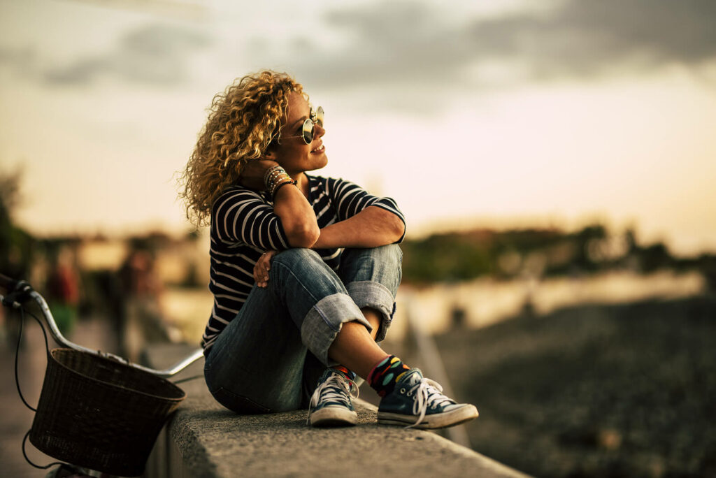 Young African American woman happily sitting on a wall overlooking the city. You can be successful in this journey with ADHD, there is hope! ADHD focused therapy in NYC can teach you how to manage the symptoms of ADHD to your advantage! Learn more here.