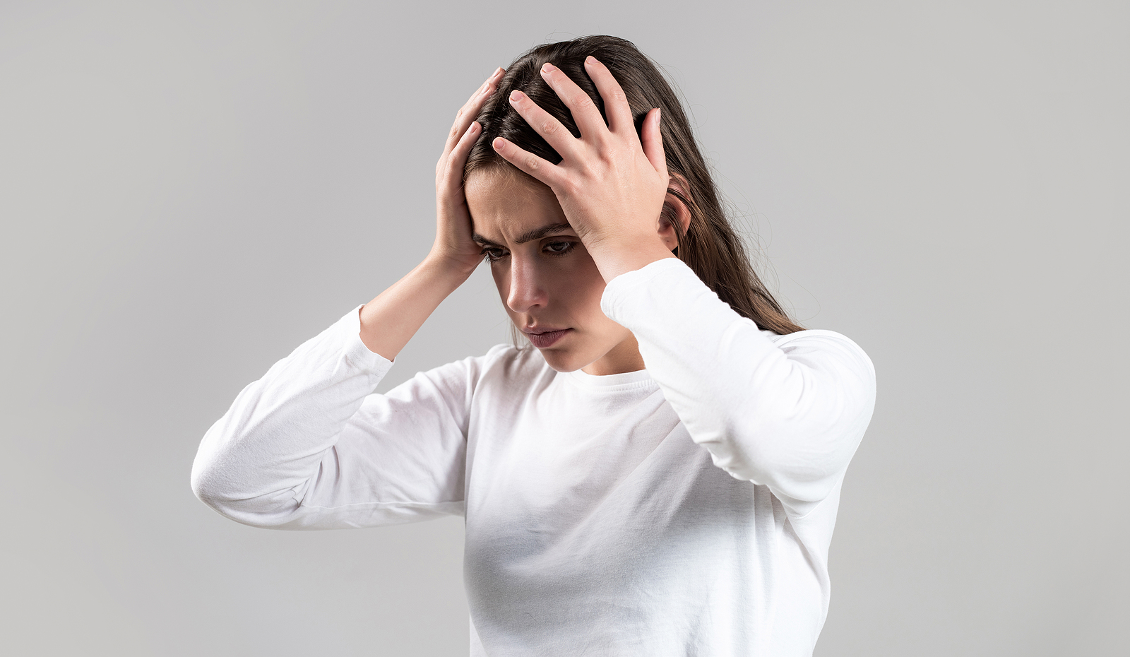 Brunette woman touching her temples feeling stress, on gray background representing dealing with ADHD. Are you struggling with the challenges that come with ADHD? Feeling stuck and overwhelmed? ADHD focused therapy in NYC can give you the tools to move forward successfully by embracing your ADHD.