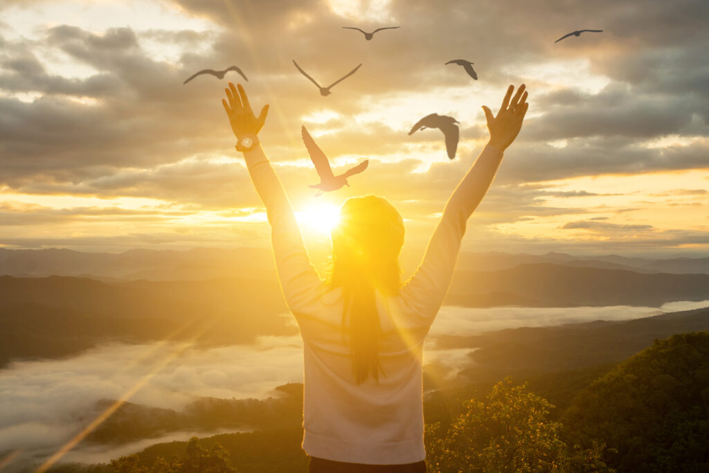 Photo of a woman holding her hands up during sunset with birds flying over her. Living with the symptoms of ADHD can be difficult. With ADHD treatment in NYC you can learn how to manage your symptoms easier. Learn more here. 