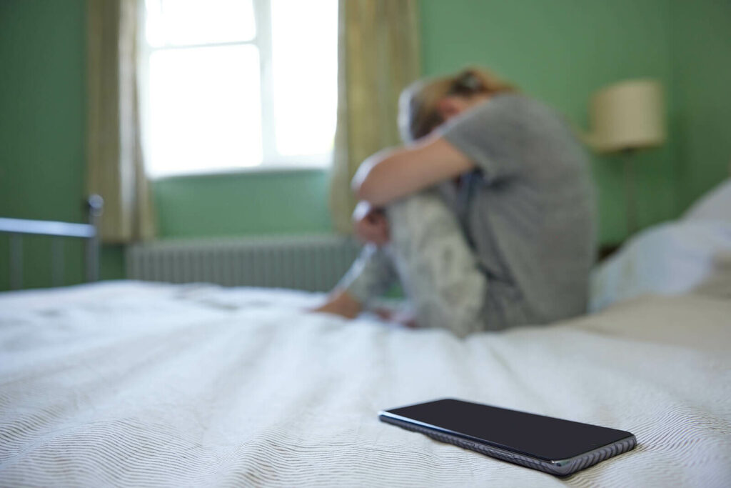 Woman sitting on her bed with her phone pushed away representing someone who is struggling to overcome Social Anxiety and ADHD. Reconnect with the world with ADHD-Focused Therapy for Anxiety in NY, NY.