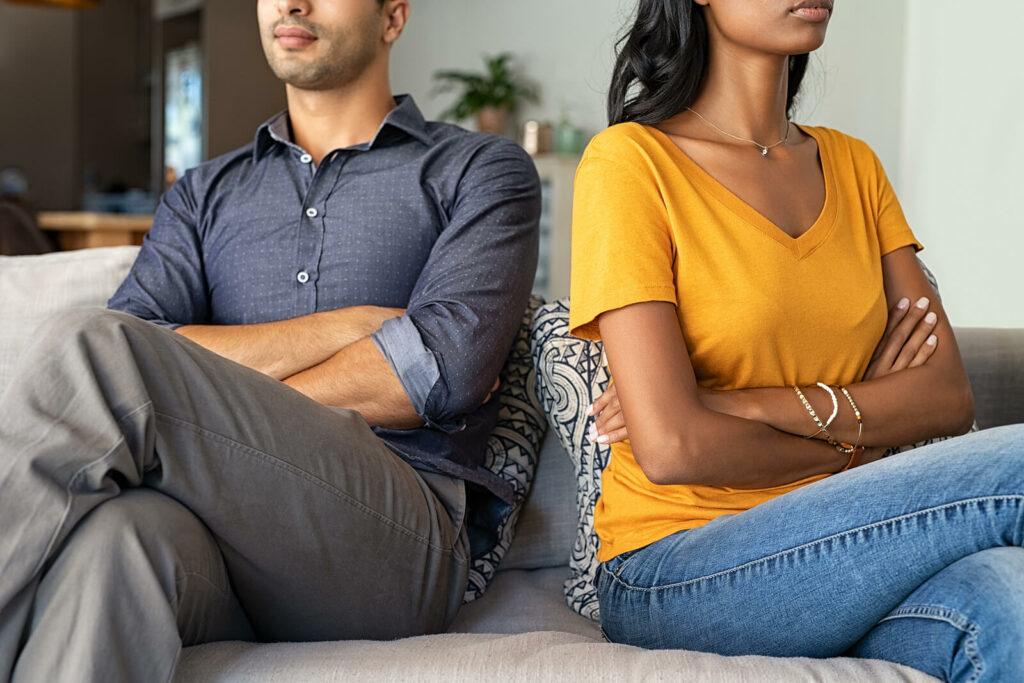 Man and a woman sitting on a couch with their backs to each other representing the challenges that can come with ADHD in relationships. ADHD-Focused Couples Therapy in NYC can help navigate these challenges.