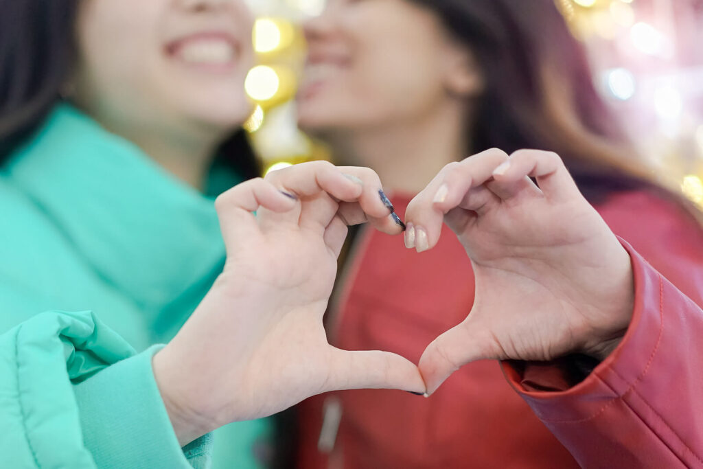 Happy lesbian couple making a heart with their hands representing a couple who has overcome their struggles with ADHD through ADHD-Focused Couples Therapy in NYC.