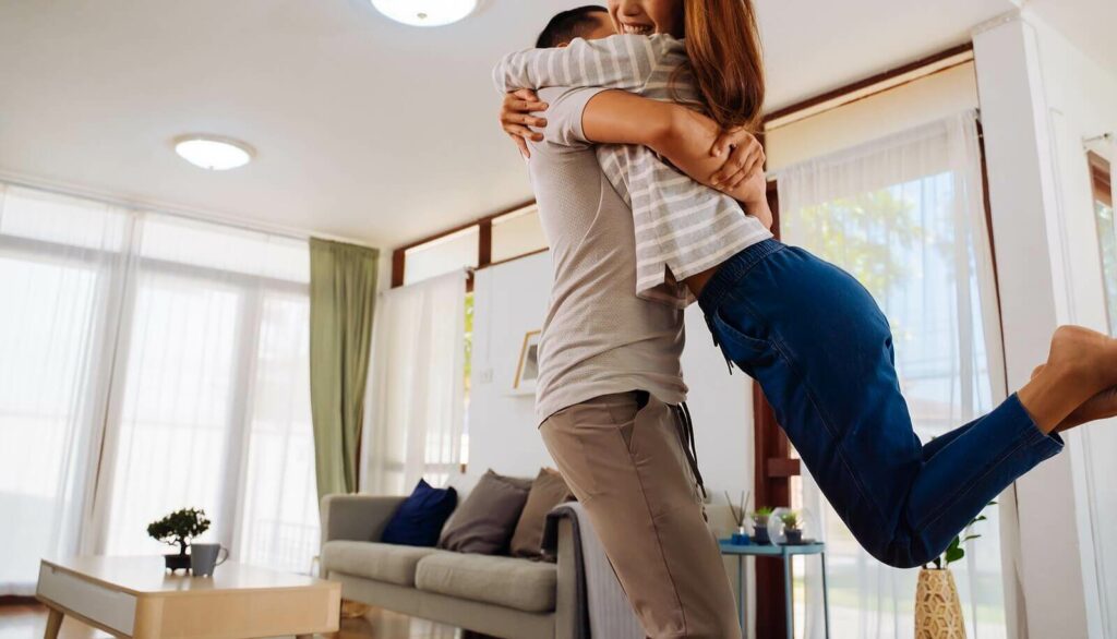 Asian couple embracing happily in their living room representing the peace that can be found in your relationship with ADHD-Focused Couples Therapy in NYC.