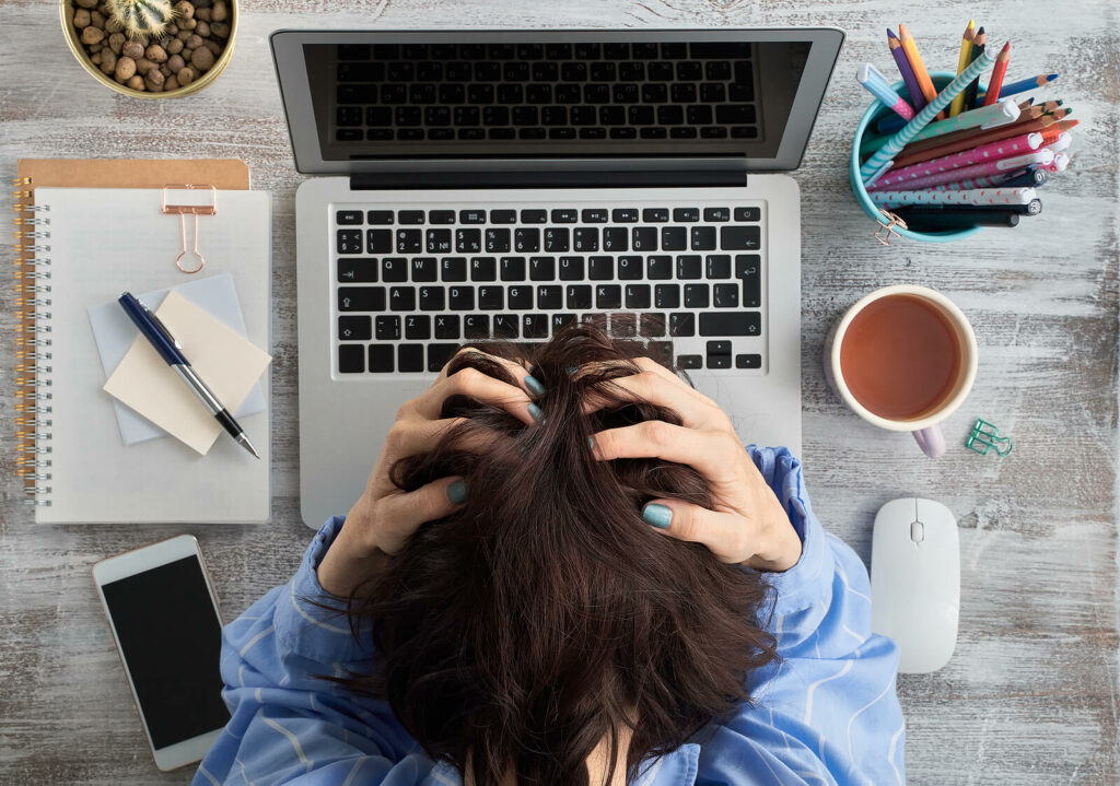 Woman sitting with her head in her hands at her desk struggling with her symptoms of her ADHD. If you are struggling ADHD Focused Therapy can help.