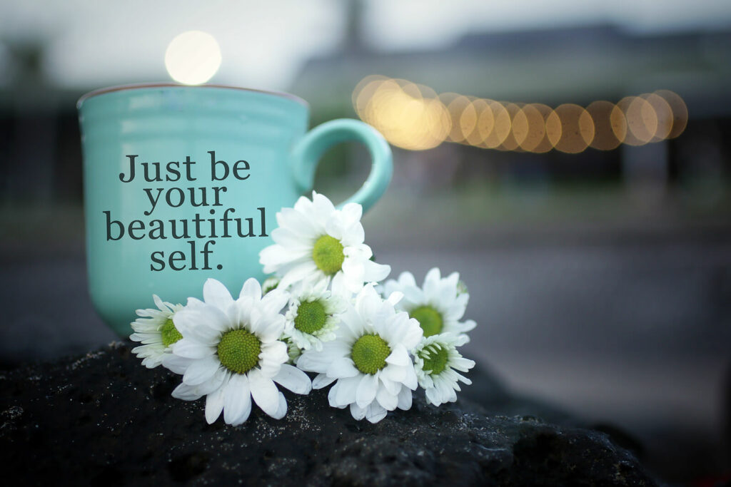 White flowers with a blue coffee cup sitting next to it that says "Just be your beautiful self" representing the need to accept and embrace your ADHD diagnosis with the help of ADHD-Focused Therapy in NYC.