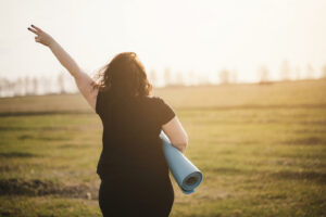 A person holds up a peace sign while walking across a field with a yoga mat. Learn how an ADHD therapist in NYC can support mindfulness and ADHD in New York, NY. Learn more by searching  “mindfulness adhd new york, ny” or contacting an ADHD therapist today.
